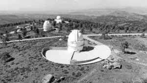 Black and white aerial view of observatory domes on a mountain landscape.